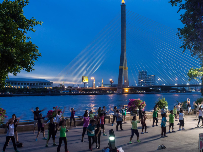 The Chao Phraya river and the King Rama VIII bridge provide a backdrop for an evening exercise class in the park
