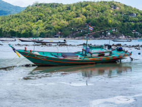 A traditional Thai longtail boat sits on the sand at low tide at Thong Nai Pan Yai beach on the island of Koh Phangan
