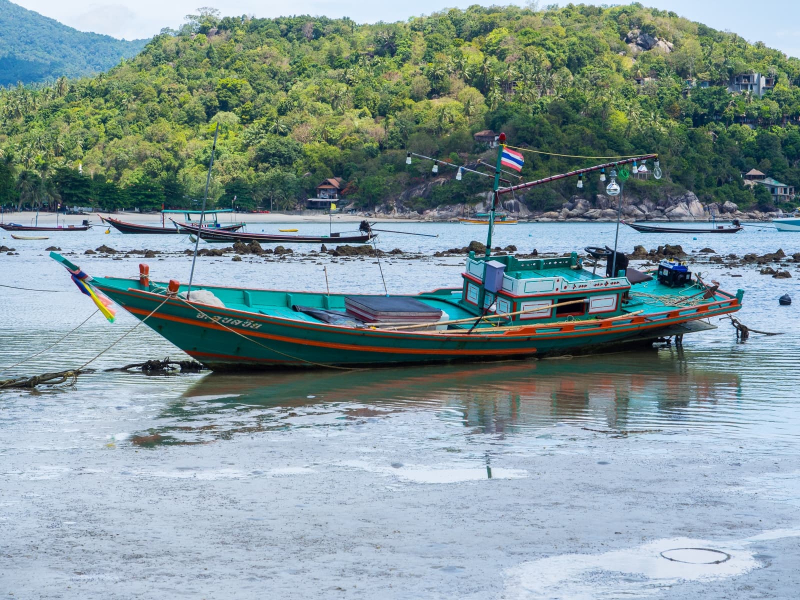 A traditional Thai longtail boat sits on the sand at low tide at Thong Nai Pan Yai beach on the island of Koh Phangan