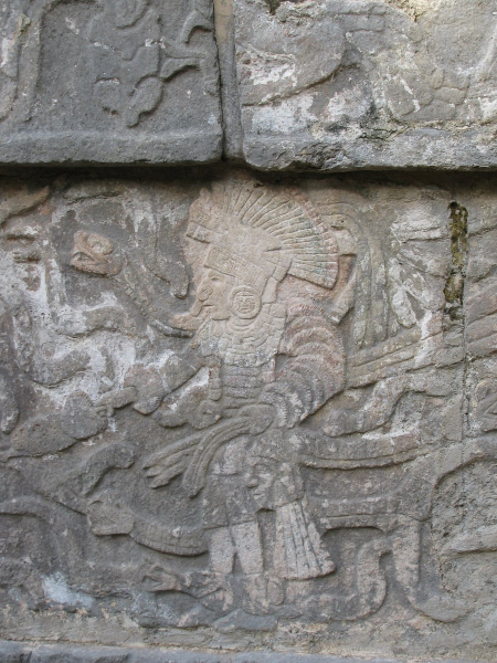 A carved figure in an elaborate headdress holding a human head and surrounded by serpents