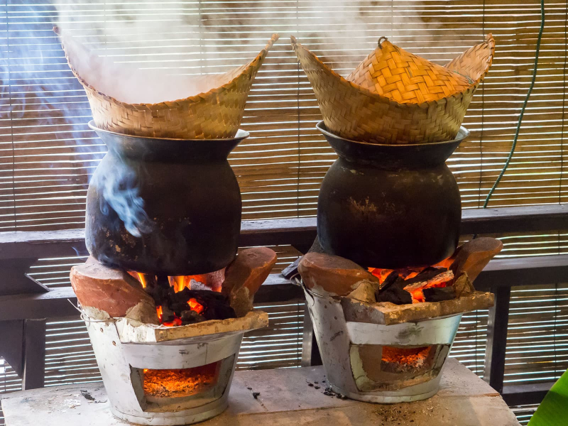 Cooking sticky rice in a bamboo steamer over a pot of boiling water on a brazier