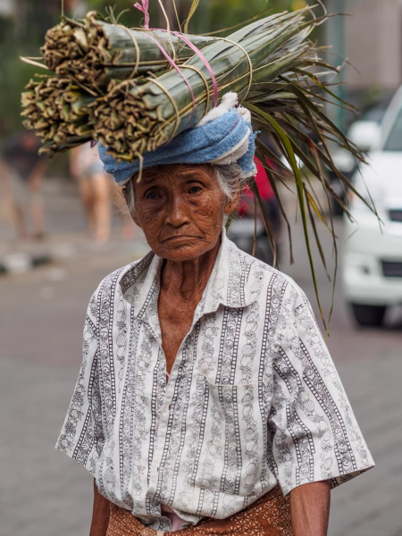 A woman carries the kind of palm leaves used to weave offering baskets