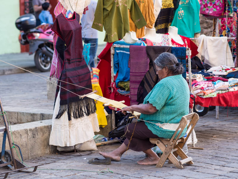 A clothing vendor weaving on a backstrap loom