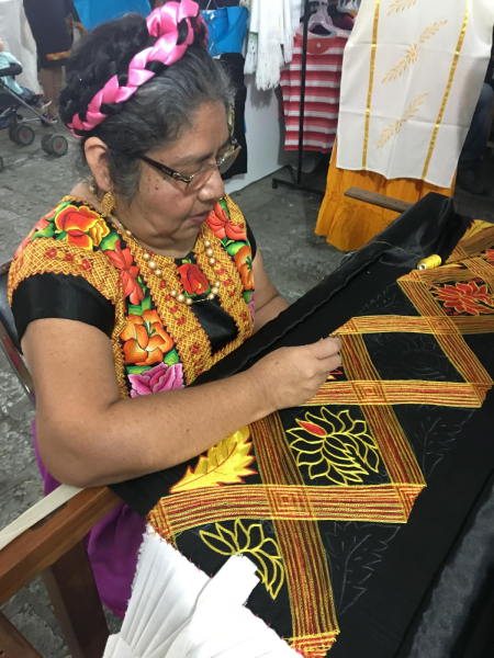 A village woman in traditional festival dress embroiders cloth in a special Christmas market