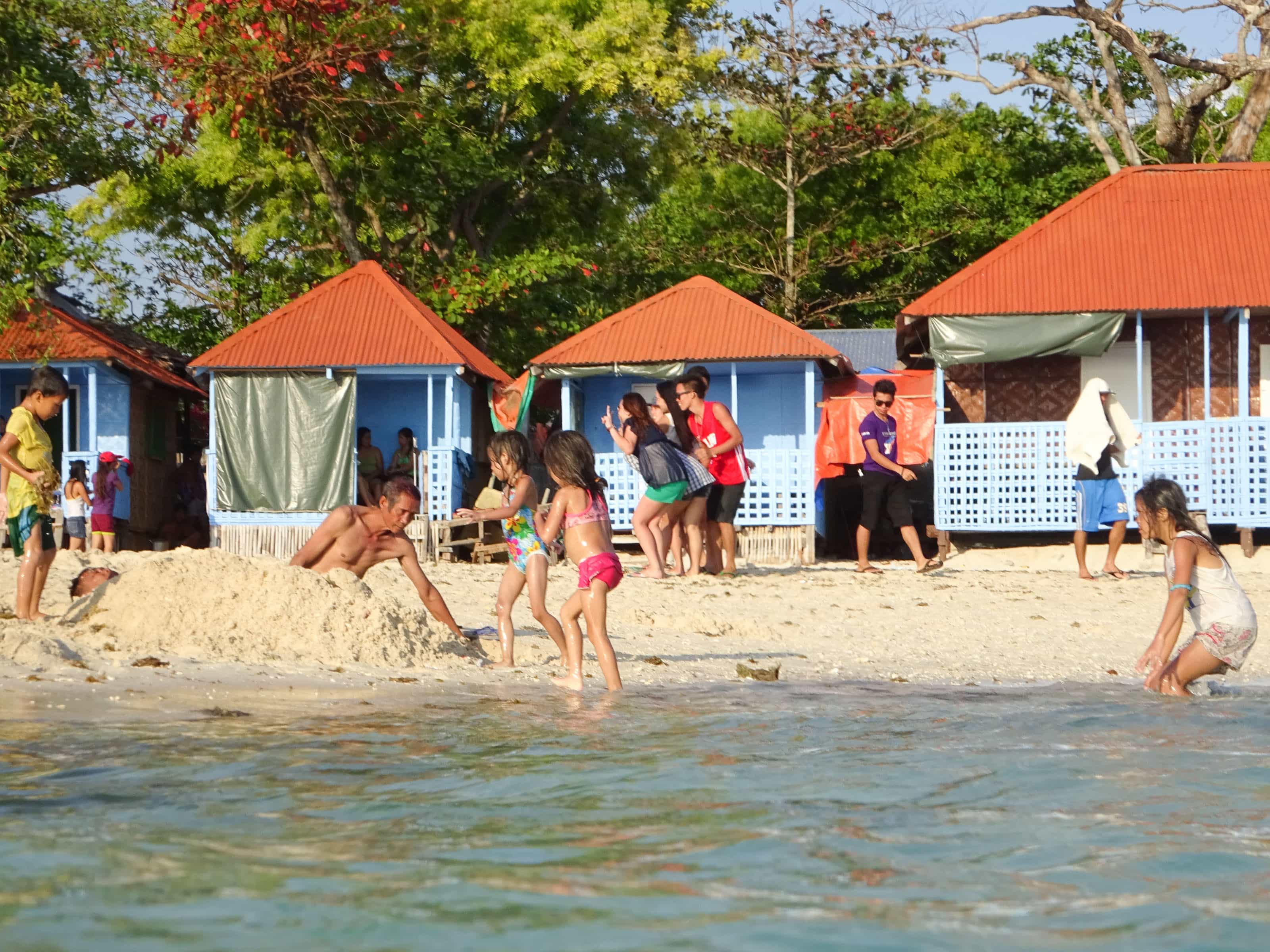 People playing on beach in front of little cottages