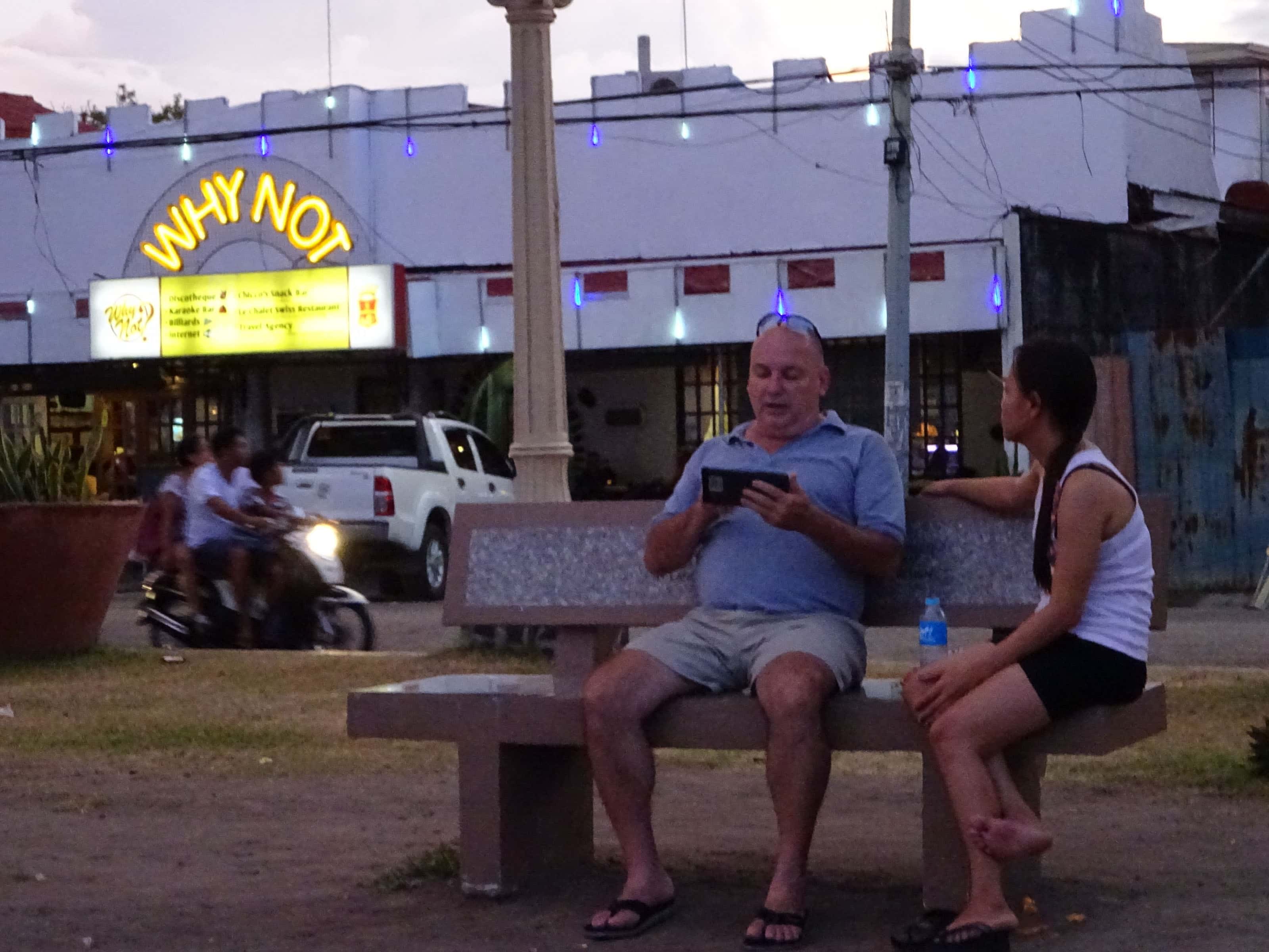 Middle-aged Western man sitting on bench with younger Filipino woman