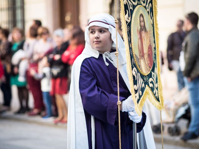 Boy in purple and white robes holding banner with picture of Jesus