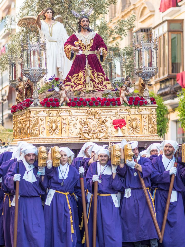 People in purple robes carry gold float with figures of kneeling Jesus and an angel behind him
