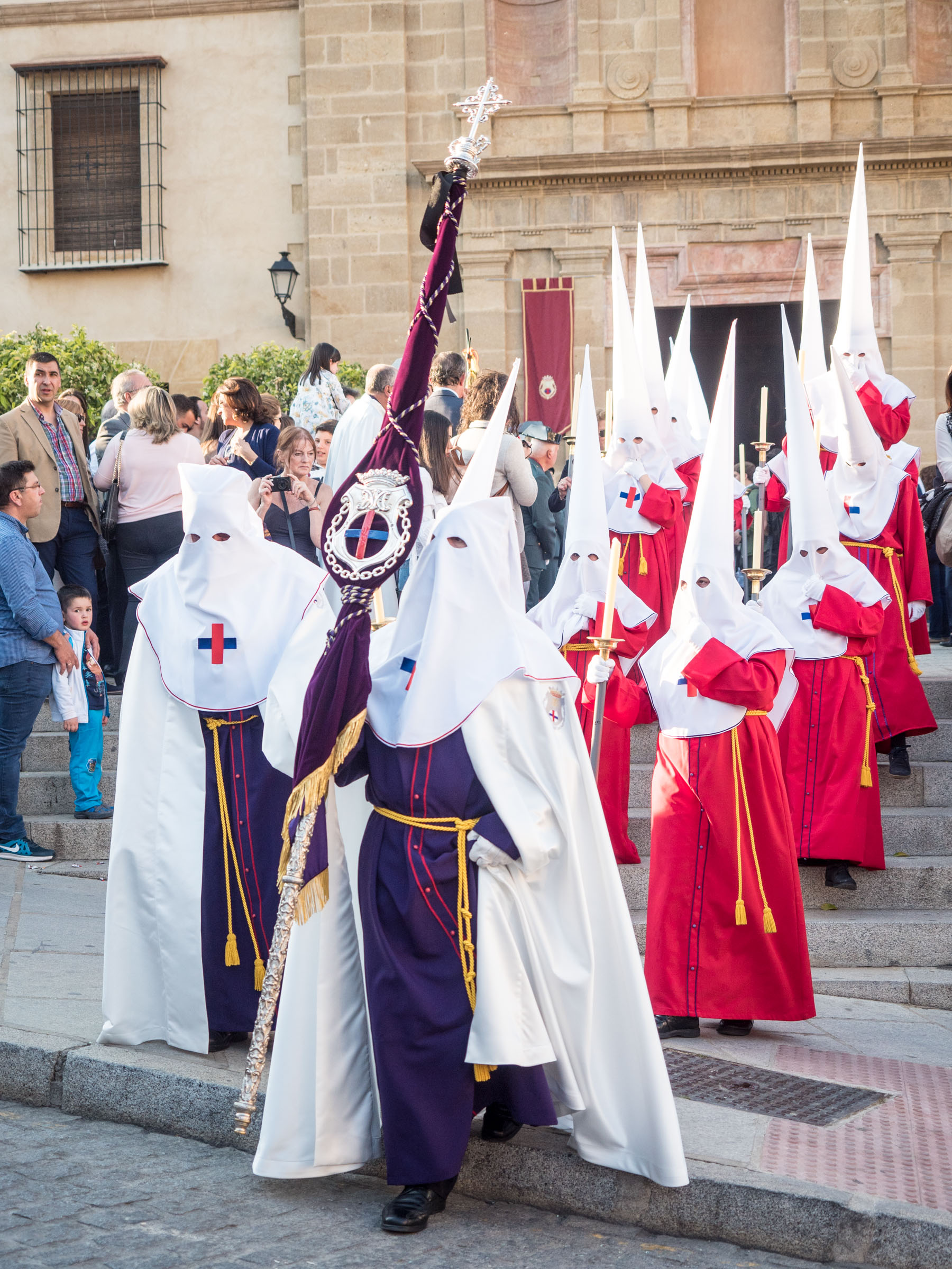 Nazarenos in red or purple robes and white pointed hoods with eye slits