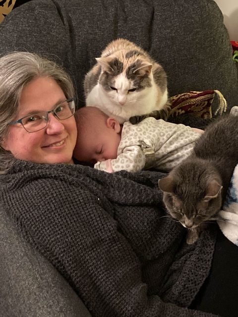 Melissa with a baby and two cats on her lap