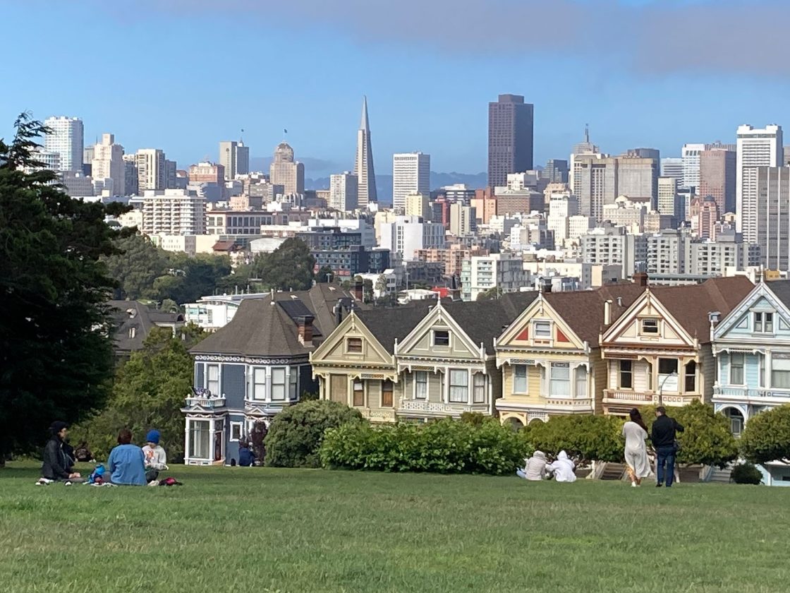 People sitting in Alamo Square park with view of "Painted Ladies" and downtown skyscrapers
