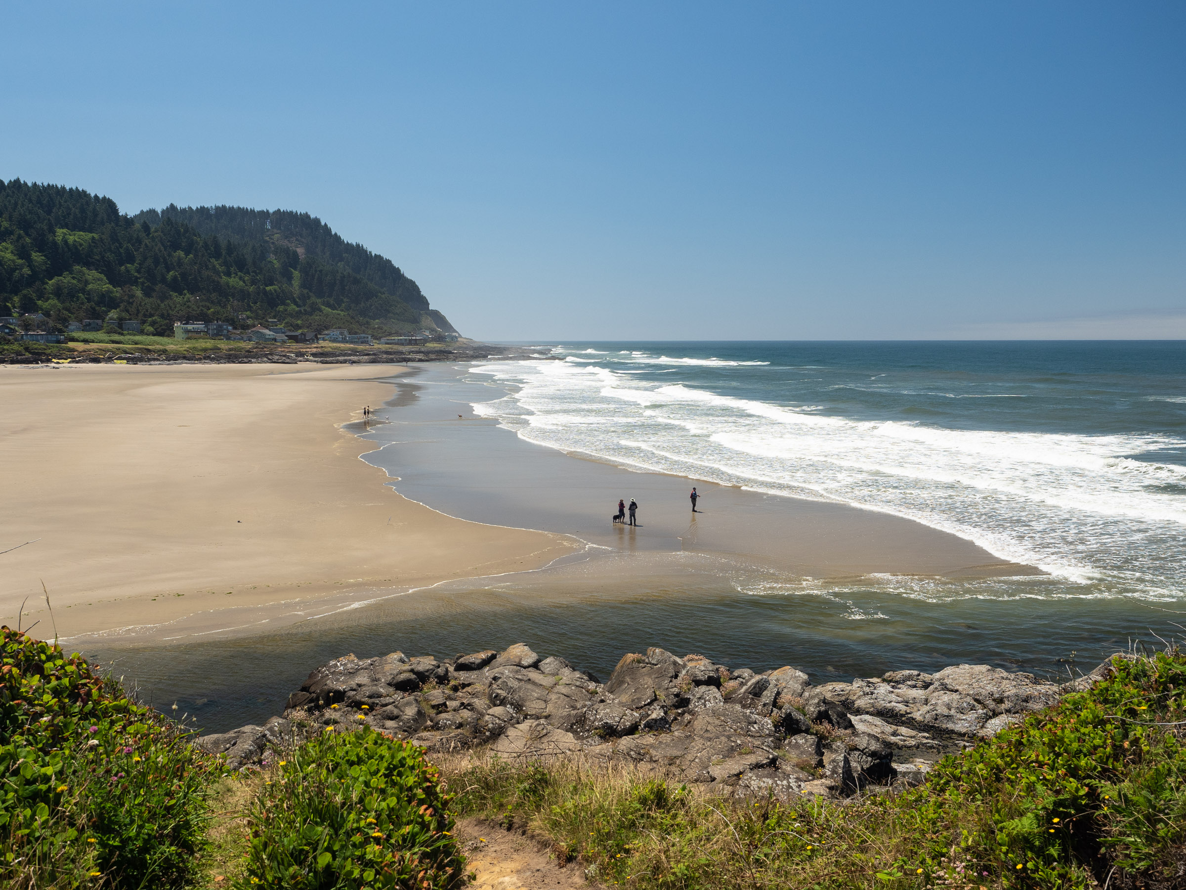 Wide sandy beach with white surf and green hills on the sides