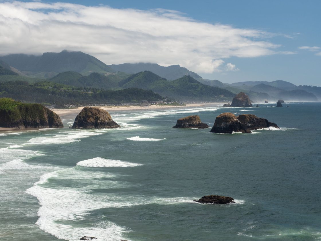 Beach with waves, sea stacks, distant mountains, and clouds