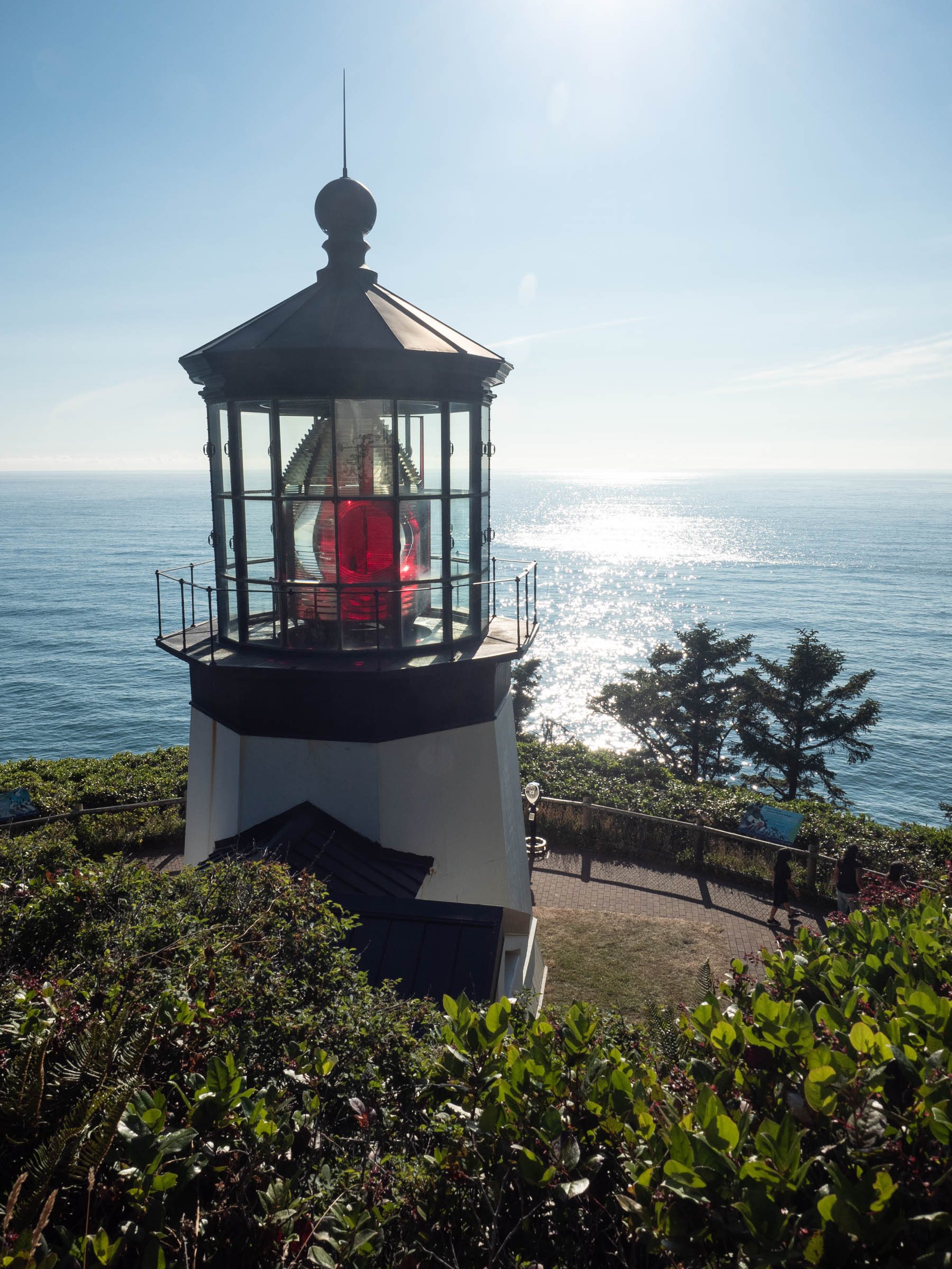 Top of lighthouse with red lantern bulb and sunlit ocean behind it