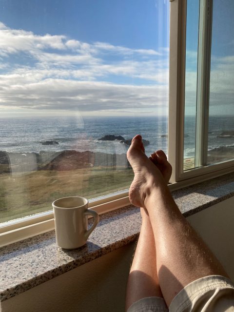 Big window with ocean view, with feet and a mug on the windowsill