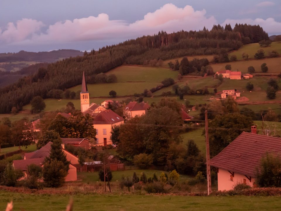 Village of St. Racho with church spire amid green fields in rosy late-day light