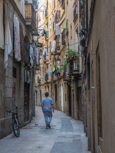 Man in blue shirt walking down narrow street lined with buildings
