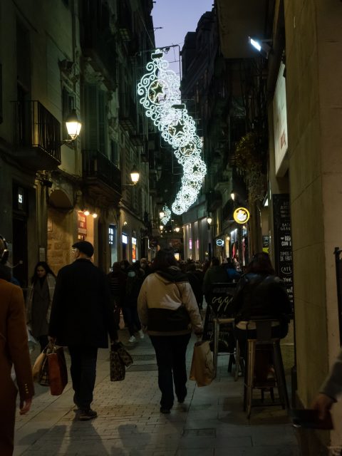 Shoppers walking down a dark, narrow street with Christmas lights 