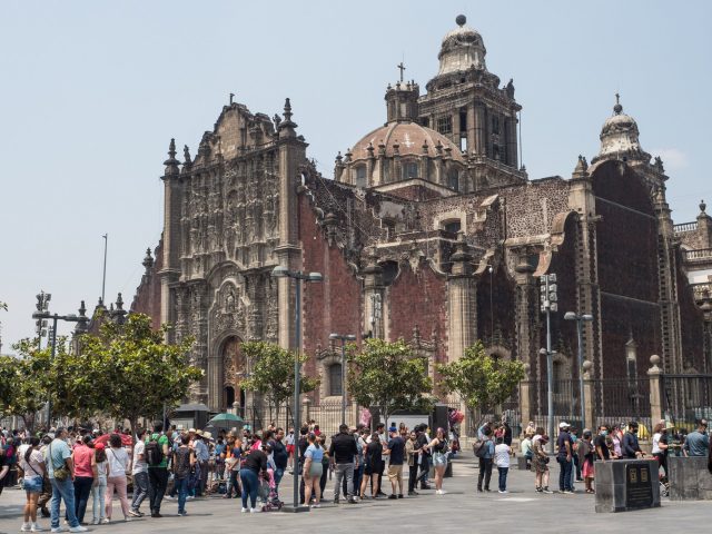 People lined up in front of red stone Baroque church
