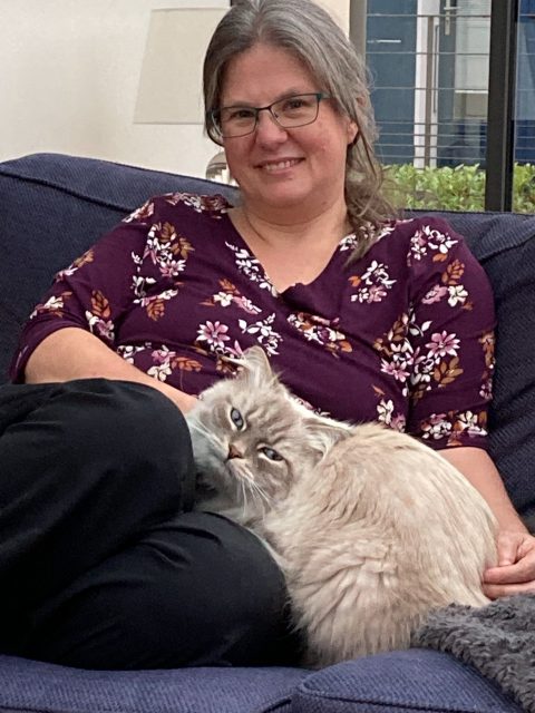 Melissa sitting on a sofa petting a fluffy white and gray cat