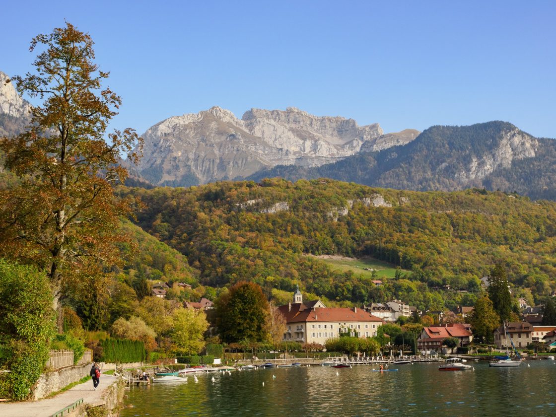 Curve of small bay on the lake with large stone hotel building, forested hills, and high mountains behind it for