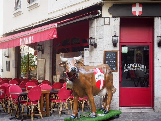 Statue of brown cow with Savoy flag on it (red field with white cross) in front of restaurant called O Savoyard!