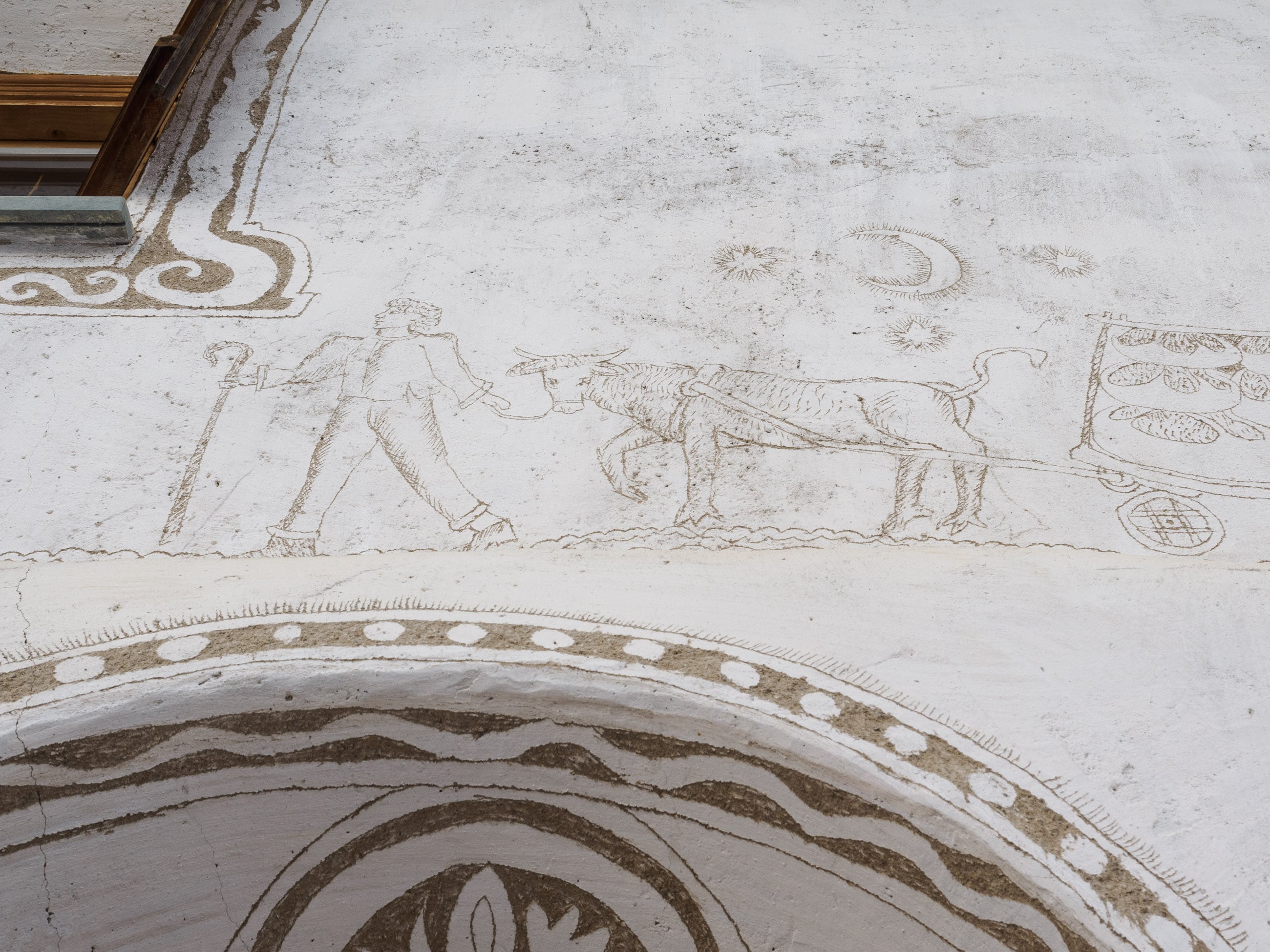 Sgraffito etching on a house in Sent of a walking man leading an ox cart full of bread loaves