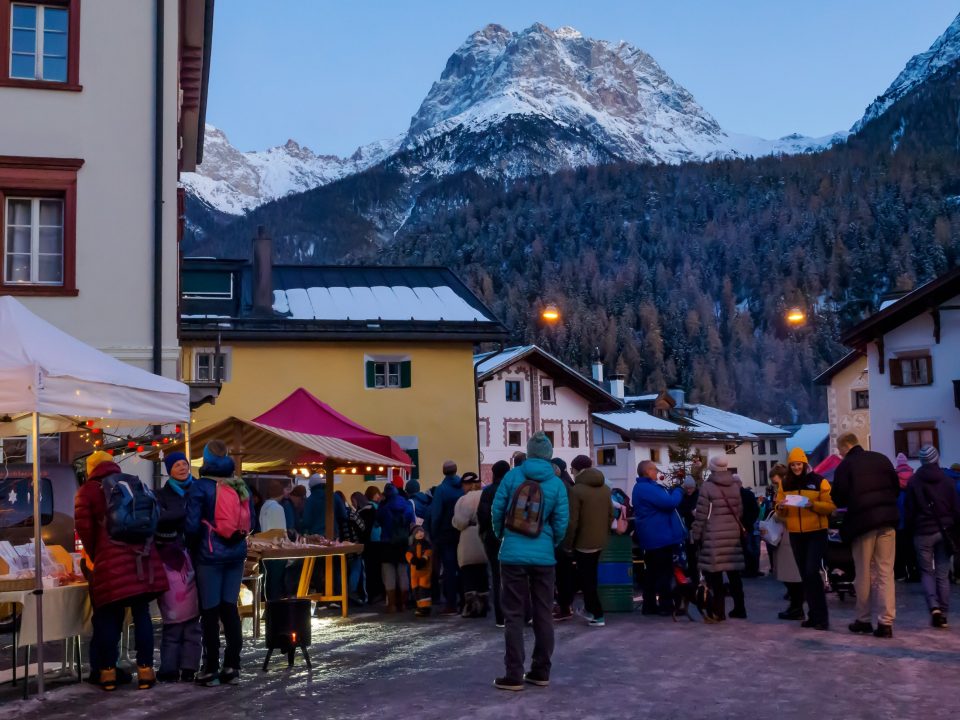 People in winter coats at an outdoor Christmas market in Scuol