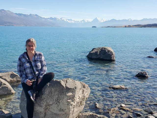 Melissa on a rock in front of blue water with white mountains in the distance